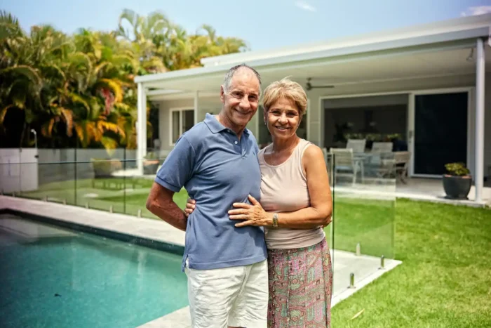 Mature Australian homeowners coupled and standing in front of pool at rear of their suburban property